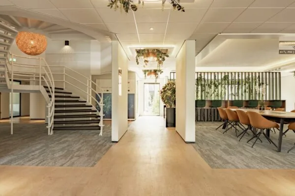 Moderne en licht ingerichte kantoorruimte met een open trap, vergadertafel en plantenwand aan de Burgemeester Verderlaan.